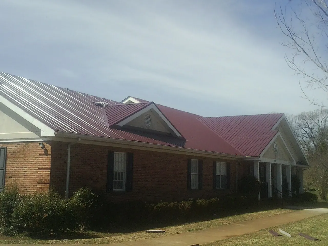 Red metal roof with gabled entries on a long brick building, from a Hail Damage Roof Repair job in Colfax